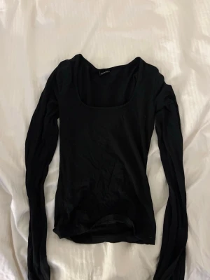 Svart långärmad topp med rund hals - En stilren svart långärmad topp med rundad, djup urringning. Perfekt att matcha med jeans eller kjol för en enkel och snygg look. Tunn och mjuk i materialet, sitter nära kroppen.