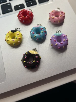 6 st Färgglada donut-berlocker - Söta berlocker formade som donuts i olika färger med strössel. Perfekta att använda som smyckesdetaljer till halsband, armband eller nyckelringar. Tillverkade i plast med metallögla för enkel fastsättning.