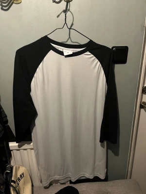 Gymshark baseballtröja svart/vit - Snygg baseballinspirerad oversized t-shirt från Gymshark med svarta ärmar och vit front och rygg. Stort tryck med texten 'GYMSHARK BODYBUILDING' på ryggen. Perfekt för dig som gillar sportig stil. Tröjan är limiterad så inte lika vanligt att få tag på! 