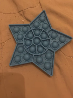 Blå stjärnformad pop it-leksak - En blå pop it-leksak i mjukt silikon, formad som en stjärna. Perfekt för att stressa ner eller bara ha något att pilla med. Leksaken har flera bubblor att trycka på och är enkel att ta med sig överallt.