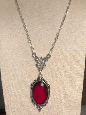 Silverhalsband med röd sten - Snyggt halsband i silverfärgad stål med en stor oval röd kristall i mitten. Hänget har en vintageinspirerad ram med detaljerade mönster och kedjan är medelgrov. Perfekt för dig som gillar statement-smycken och vill sticka ut.