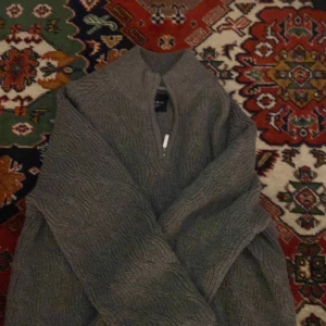 Grå stickad tröja med halv dragkedja - Säljer en grå stickad tröja från Bondelid med halv dragkedja framtill och diskret mönster i stickningen. Tröjan har hög krage och är perfekt för dig som gillar klassisk men avslappnad stil.