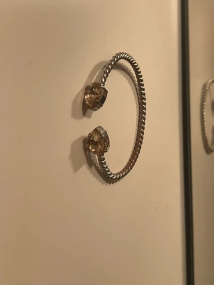 Silvrigt armband från Carolina svedbom - Säljer ett öppet armband i silverfärgad metall med tvinnad design. Armbandet har två stora stenar med bärs färg ❤️