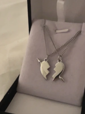 Silverfärgat vänskapshalsband hjärtan - Två silverfärgade halsband med varsin halva av ett hjärta som tillsammans bildar två narvaler. Hängena har en cool, kantig design och kedjorna är tunna och stilrena. Perfekt för att dela med en vän eller partner.