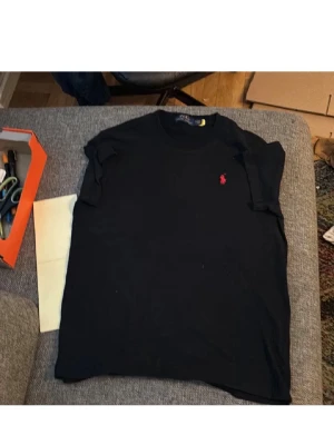 2-pack t-shirts från Ralph Lauren - Två klassiska t-shirts från Ralph Lauren, en svart med röd logga och en vit med marinblå logga. Båda har rund halsringning och kort ärm, tillverkade i mjuk bomull. Perfekta för en clean och stilren look.