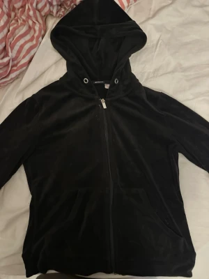 Svart velour hoodie med dragkedja - Mysig svart hoodie i mjuk velour med dragkedja framtill och två fickor. Klassisk huva och långa ärmar, perfekt för en chill och avslappnad stil. Passar till allt och är superbekväm att ha på sig.