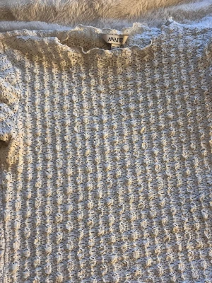 Vit ribbad topp från AWARE - Supersöt vit topp från AWARE med ribbad struktur och lätt volangkant vid halsen. Materialet är stretchigt och har en unik textur som ger toppen en trendig look. Perfekt att styla med jeans eller kjol för en fräsch outfit.