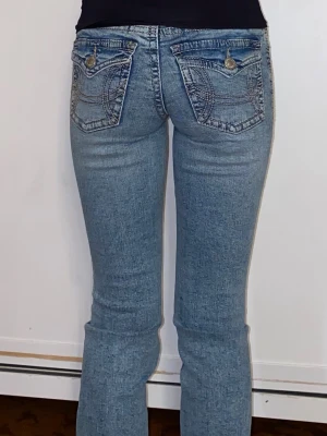 Ljusblå bootcut jeans med design på fickorna - Säljer ett par ljusblå jeans bootcut från ginatricor med snygga detaljerade bakfickor med knappar. Jeansen har normal midja i strl 32, men passar 32/34. Helt nya, köpte igår för 499kr och endaste provade. Säljer då jag inte vet om jag tycker om de😊