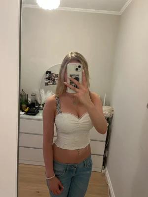 Vit spetsig tube top Urban Outfitters - Säljer en vit, figurnära tube top från Out From Under för Urban Outfitters. Toppen är axelbandslös och är täckt av spets. Perfekt till jeans eller kjol för en trendig look.