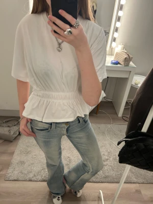 Vit topp med resår och volang - Säljer en söt vit topp med korta ärmar, resår i midjan och volang nedtill. Toppen har en avslappnad passform och är gjord i ett mjukt material. Perfekt att styla med jeans eller kjol för en trendig look. Säljer denna jättefina topp då den ej kommer till användning och har endast haft den ca 4 gånger. Djur och rökfritt hem! I storlek S från lager 157. Nypris: 150kr! (Säljs ej längre🙂