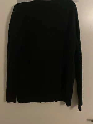 olo Ralph Lauren stickad tröja - Klassisk svart stickad tröja från Polo Ralph Lauren med rund halsringning och röd broderad logga på bröstet. Tröjan har långa ärmar och ribbade muddar vid ärmslut och nederkant. Perfekt till höst och vinter för en stilren look. Pris kan diskuteras!