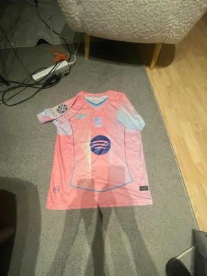 Rosa Nike FC Barcelona matchtröja - Säljer en rosa och ljusblå FC Barcelona matchtröja från Nike med Dri-FIT ADV-teknologi. Tröjan har klubbmärke, sponsorlogga och Champions League-märke på ärmen. Perfekt för dig som älskar fotboll och vill sticka ut på planen.