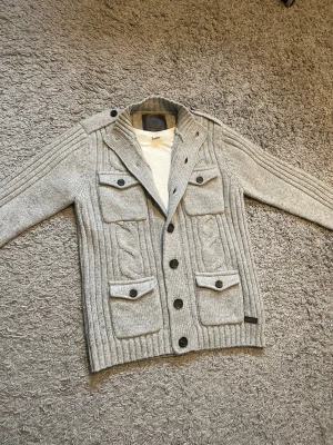 Grå stickad cardigan  - Säljer en trendig stilren grå stickad ull cardigan, med fickor! 🙌🏻Perfekt nu för kommande kalla dagar! ✨Plagget är i nyskick 9,2/10. Tröjan har en klassisk knapp öppning upp till, med en stil som siktar på ”oldmoney” och ”vintage”, men passar till det mesta!🤩 Tveka inte på att höra av er!💪🏼