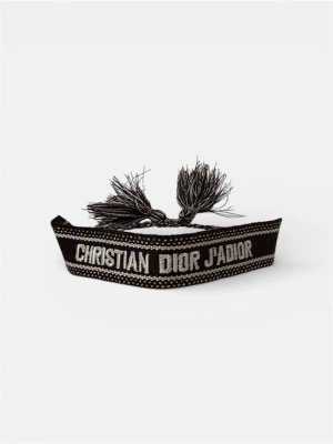 Christian dior armband - Ett elegant och stilfullt armband från Christian Dior med den ikoniska "J'ADIOR"-loggan. Armbandet är gjort i en svart textilstil med vita bokstäver och inslag av små guldfärgade pärlor som ger en lyxig känsla. De fina fransarna/tofsarna på sidorna bidrar till designens charmiga utseende. Perfekt för att addera en touch av glamour till vilken outfit som helst!