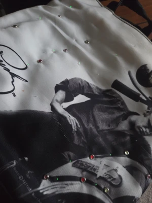 Shoppingväska med Elvis print. - Cool shoppingväska i vitt tyg med svartvit fotoprint av en person på motorcykel och dekorativa små stenar. Väskan har svarta handtag i syntetmaterial och en unik design som sticker ut.