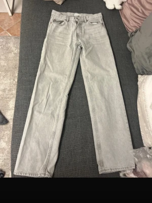 Grå jeans , rak modell - Säljer ett par grå jeans  i rak modell. De har klassisk femficksdesign, bälteshällor och knappstängning fram. Materialet är jeans och färgen är ljusgrå, vilket ger en clean och stilren vibe. Passar dig som gillar enkel och tidlös stil.