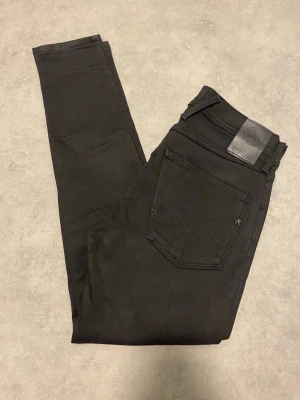 Helt nya Replay Anbass svarta jeans - Svarta Replay Anbass jeans med slim passform och klassisk femficksdesign. Jeansen har svarta sömmar, Replay-logga på fickan och läderpatch bak i midjan. Materialet är stretchigt jeans och modellen är smal med normal midja.