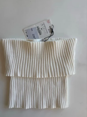 Vit ribbad bandeau tubtopp - Säljer en vit bandeau tubtopp från By Malene Birger i storlek S. Toppen är ribbad och har en snygg, strukturerad look med breda ribbor. Perfekt för att styla med jeans eller kjol för en trendig vibe.