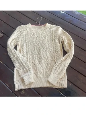 Beige stickad tröja från Part Two - Säljer en beige stickad tröja från Part Two i storlek S. Tröjan har ett snyggt kabelstickat mönster med detaljer på både fram- och baksida samt ribbade muddar vid hals, ärmslut och nederkant. Perfekt för kyliga dagar och enkel att styla med jeans eller kjol.