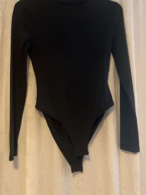 Svart långärmad bodysuit - Säljer en svart långärmad bodysuit med rund hals. Modellen är tight och har en enkel, stilren design utan synliga detaljer. Perfekt att styla med jeans eller kjol för en clean look.