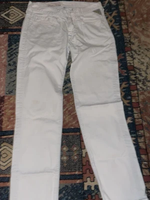 Vita jeans från Replay - Säljer ett par fräscha vita jeans från Replay med klassisk femficksdesign och ljusblå sömmar. Jeansen har rak passform och är tillverkade i mjukt bomullsmaterial. Perfekta för dig som vill ha en clean och stilren look.