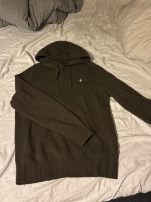 Olivgrön hoodie från Morris, M - Snygg olivgrön hoodie från Morris med huva och snörning. Tröjan är i mjuk bomull och har ribbade muddar vid ärmslut och nederkant. Klassisk passform och diskret Morris-logga på bröstet. Perfekt för en chill och stilren look. Helt ny knappt använd. Lapp och allt finns