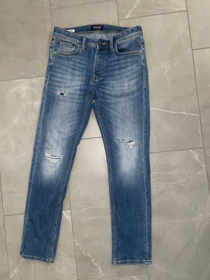 Blåa jack&jones jeans - Säljer ett par otroligt feta jack & Jones jeans med slitningar, skick: 8,5/10=mycket bra. Modell: tapered/mike. Storlek: W30/L32. Hör av er vid minsta frågor och fundering 😄