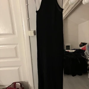 Svart långklänning från Pull&Bear - Hej! Säljer min svart långklänning från Pull&Bear i storlek S. Klänningen är ärmlös med smala axelband och har en lätt transparent stickad struktur som gör det till en prefekt strandklänning, den har även en slits vid höger ben. Den är lite pösigare och väldigt lång. Aldrig använd. Hör av er vid frågor🥰