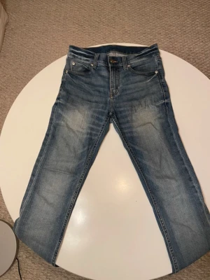 Cheap Monday blå jeans, storlek 26/32 - Snygga Cheap Monday  jeans i klassisk blå tvätt med lätt slitning på låren och raka ben. Jeansen har fem fickor, silverfärgade nitar och brunt läderpatch bak. Passformen är slim och materialet är robust denim i bomull.