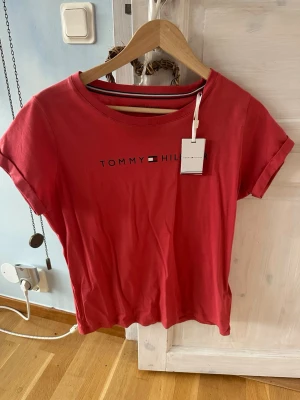 Rosa t-shirt Tommy Hilfiger S - Snygg rosa t-shirt från Tommy Hilfiger i mjuk bomull. Klassisk rund hals och korta ärmar med uppvik. Framsidan har stilrent tryck med logotypen. Perfekt för dig som gillar enkel och trendig stil med en touch av premium.