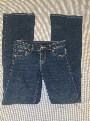 Blå raka jeans med klassisk look - Snygga blå jeans med vida ben och klassisk femficksdesign. Jeansen har kontrastsömmar och knappstängning fram. Passar dig som gillar en tidlös och enkel stil. Materialet är slitstarkt jeans och färgen är mörkblå med lätt tvättad effekt.