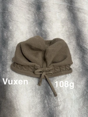 Brun stickad mössa med snörning - Säljer en brun stickad mössa med snygg snörning framtill och ett flätat mönster längs kanten. Mössan har en mjuk och skön känsla.. Passar dig som gillar en chill och enkel stil.🌸Fint använt skick. Storlek vuxen