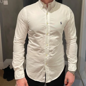Vit skjorta från Ralph Lauren - Säljer en vit Oxford skjorta från Ralph Lauren med button-down krage och broderad logga på bröstet. Skjortan har slim passform och är tillverkad i mjuk bomull. Utmärkt skick! 