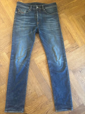Blå Diesel jeans med tapered fit - Säljer ett par blå jeans från Diesel med snyggt slitna detaljer och klassisk femficksdesign. Jeansen har slim passform och normal midja, vilket ger en modern och avslappnad look. Materialet är robust denim i bomull och de har en diskret Diesel-logga på bakfickan.