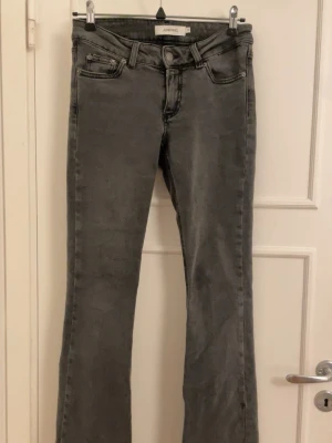 Bootcut jeans från Junkyard XS - Snygga grå bootcut jeans från Junkyard i storlek XS. Jeansen har en klassisk femficksdesign, är mid rise och har råa kanter vid bensluten för en cool vibe. Materialet är jeans med en lätt tvättad look och svarta sömmar som ger extra edge.