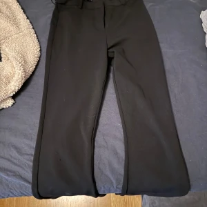 Svarta vida kostymbyxor - Säljer ett par svarta kostymbyxor med vid passform. Byxorna har en klassisk look med raka ben och hög midja. Perfekta att styla med sneakers eller boots för en clean vibe. Materialet känns mjukt och följsamt.