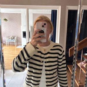 Randig kofta från Gina Tricot - Säljer en stickad kofta från Gina Tricot i svart och vit med breda ränder. Koftan har snygga guldfärgade knappar med emblem, två små fickor framtill och ribbade muddar. Perfekt för lager-på-lager och chill stil.