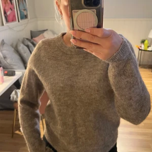 Gråbrun stickad tröja från Lindex - Mysig gråbrun stickad tröja från Lindex med rund halsringning och långa ärmar i 46% ull.