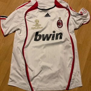 AC Milan Champions League tröja Adidas - AC Milan fotbollströja från Adidas, Champions League-finalen 2007 edition. Vit med röda och svarta detaljer, klubbmärke och Bwin-tryck på bröstet. Korta ärmar och tillverkad i lätt funktionsmaterial, perfekt för fotboll eller samling.
