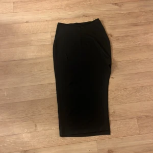 Svart medellång kjol från SHEIN - En stilren svart medellång kjol från SHEIN i figurnära modell. Kjolen är tillverkad i mjuk och stretchig polyesterblandning och har en klassisk, rak siluett som passar perfekt till många olika looks.