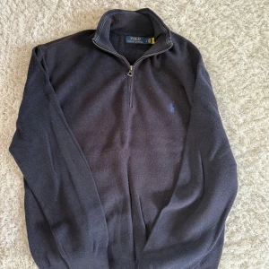 Mörkblå stickad tröja Polo Ralph Lauren - Säljer en mörkblå stickad tröja från Polo Ralph Lauren med half zip och klassisk krage. Tröjan har lång ärm och diskret broderad logga på bröstet. Perfekt för dig som gillar stilren och tidlös design.