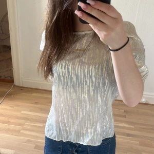 Vit och guld blus Holly & Whyte XS - Säljer en transparent vit blus från Holly & Whyte by Lindex i storlek XS. Blusen har glittriga guldiga ränder, rund halsringning och korta puffärmar. Perfekt för dig som vill sticka ut med en snygg och trendig topp!