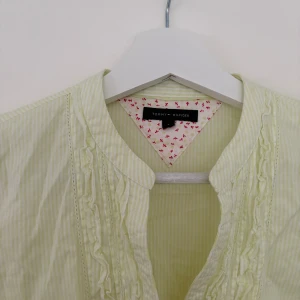 Ljusgul randig skjorta Tommy Hilfiger - Snygg ljusgul skjorta från Tommy Hilfiger med tunna vita ränder, volangdetaljer längs knappraden och klassisk krage. Långärmad och tillverkad i mjuk bomull. Perfekt för dig som gillar en fräsch och stilren look.