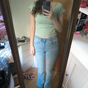 Ljusgrön croppad topp från KappAhl - Säljer en ljusgrön croppad topp från KappAhl med korta ärmar och vågiga kanter vid hals, ärmslut och nederkant. Toppen är i ribbad bomull och har en slim passform som sitter snyggt på kroppen. Perfekt för vår och sommar! Använd två gånger.