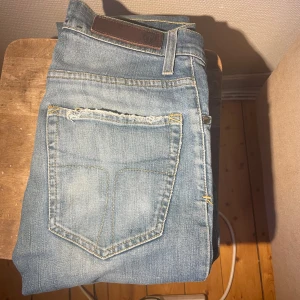 Ljusblå jeans från Tiger of Swede - Snygga ljusblå jeans från ToS med klassisk femficksdesign och brunt läderpatch bak i midjan. Jeansen har raka ben och kontrastsömmar, samt slitningar vid bakfickan för en cool, avslappnad look.