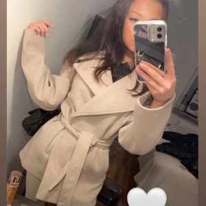 Beige kappa med bälte - Snygg beige kappa med knytskärp i midjan. Jackan har en klassisk, rak passform och långa ärmar. Perfekt för dig som vill ha en stilren och trendig look under höst och vinter. Pris kan diskuteras!