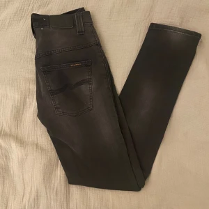 Svarta Nudie jeans - Snygga jeans från Nudie i klassisk svartgrå färg . Riktigt bra passform och tidlös stil som funkar till allt – både vardag och fest.  📏 Storlek: W27 L32 ✨ Skick: Mycket bra skick, sparsamt använda. 🧵 Material: Bomull med stretch för bekväm passform. ✅ Pris kan diskuteras