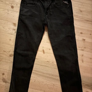 Svarta Replay jeans tapered fit - Säljer ett par svarta jeans från Replay med snyggt tvättad look. Modellen har tapered fit, klassiska fem fickor och Replay-logga på myntfickan. Jeansen är i stretchigt denim och har normal passform med avsmalnande ben. Storleken är 30/32