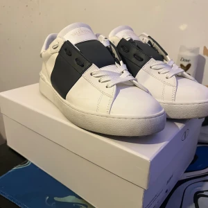 Valentino Garavani Open sneakers vit/svart - SMUTSEN PÅ SKORNA GÅR BORT FETT ENKELT. det är bara att hämta rn blöt handuk och ta bort, jag pallar ba inte. Säljer ett par snygga Valentino Garavani Open sneakers i vitt skinn med svart panel över mitten. Klassisk chunky sula, rund tå och vita snören. Märkeslogga på plös och sula. Perfekta för dig som gillar stilrena och lyxiga sneakers.