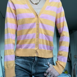 Randig kofta i gult och lila från Gant - Superfin kofta från Gant med breda orangea och rosa ränder. V-ringad med knappar hela vägen och långa ärmar. Tunn och mjuk i bomullsmix, perfekt för lager-på-lager. Snygg till både jeans och kjol!